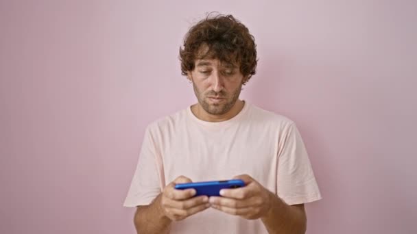 Pohledný hispánský muž zapojený do svého smartphonu na růžové zdi vyjadřující soustředění a vzrušení. - Záběry, video