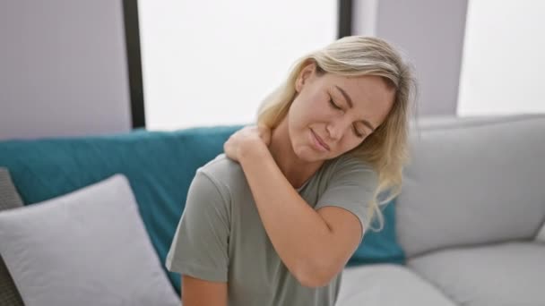 Een jonge vrouw in een casual t-shirt met ongemak of nekpijn in een moderne woonkamer. - Video