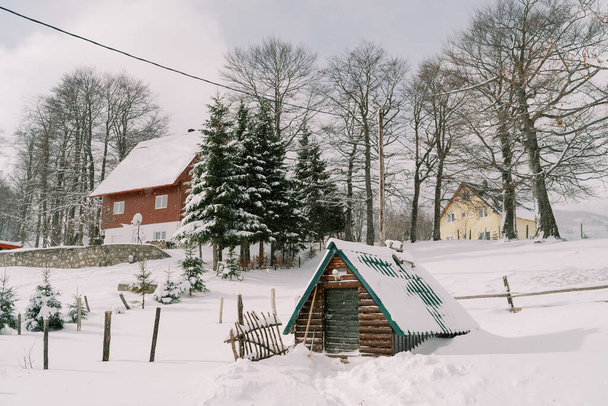 Hóval borított faház egy kétemeletes ház mellett a faluban. Kiváló minőségű fénykép - Fotó, kép