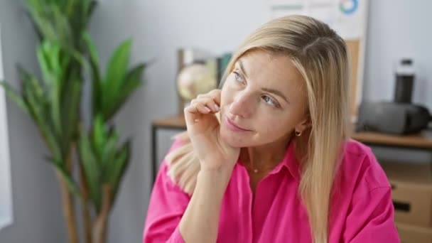 Egy figyelmes nő rózsaszín ingben pózol egy modern irodában, homályos háttérrel.. - Felvétel, videó