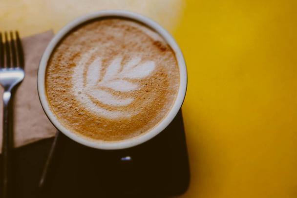 Beker van kunst latte of cappuccino koffie op een gele tafel met retro filter effect. Ontbijt warme drank boven. Herfstdrank in een mok..  - Foto, afbeelding