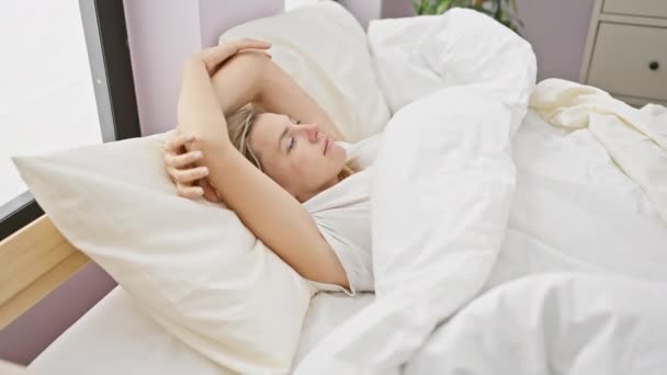 Una joven mujer caucásica contemplativa yace en la cama en casa, mostrando una mirada de estrés o consideración. - Imágenes, Vídeo