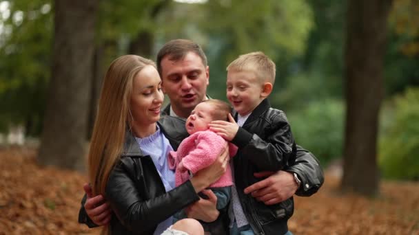 Onnellinen valkoihoinen perhe pitelee poikaansa ja tytärtään sylissään, leikkii hänen kanssaan ulkona puistossa.. - Materiaali, video