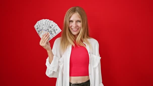 Mujer rubia sosteniendo el dinero alegremente sobre un fondo rojo - Metraje, vídeo