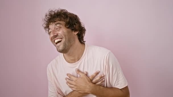 Jóképű fiatal spanyol férfi vidáman nevetett egy tömör rózsaszín háttér, felidézve a boldogság és a pozitivitás egy alkalmi portré. - Felvétel, videó