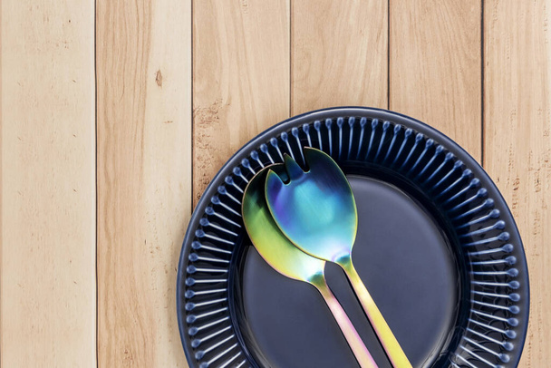 明るい青い磁器プレートと軽い木製テーブルの金属サラダカトラリー - 写真・画像
