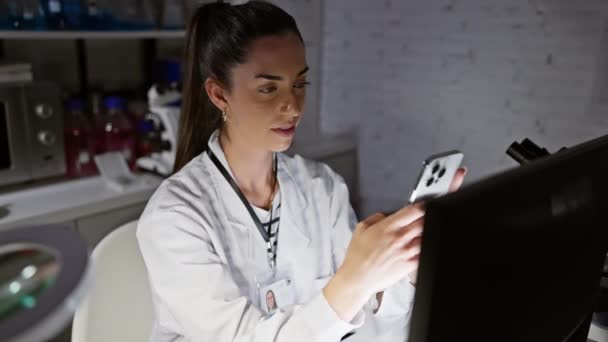 Young beautiful hispanic woman scientist using computer and smartphone smiling at laboratory - Footage, Video