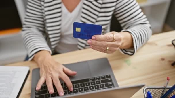 Een vrouw van middelbare leeftijd heeft een creditcard terwijl ze binnen aan haar bureau werkt.. - Video