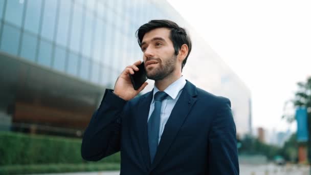 Skilled caucasian project manager calling phone while walking at city with blurred background. Skilled businessman using smart phone talking to project manager with blurred background. Exultant. - Footage, Video