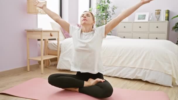 A young woman practices yoga in a serene bedroom, exemplifying health and relaxation in a personal space. - Footage, Video