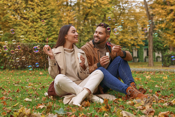Happy young couple blowing soap bubbles in autumn park - Foto, imagen