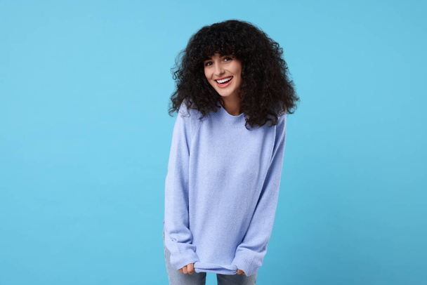 Happy young woman in stylish warm sweater on light blue background - Фото, зображення