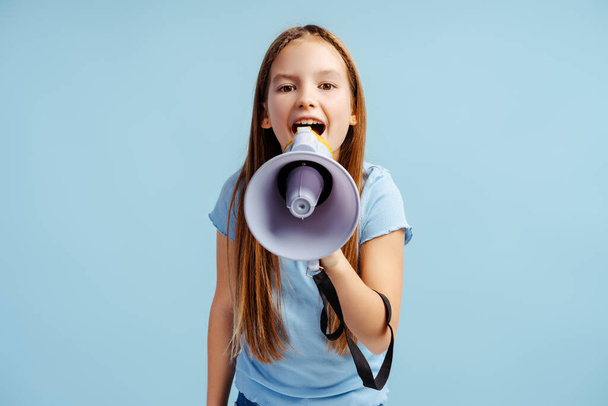 Elinde hoparlörle gülümseyen güzel bir kızın portresi mavi arka planda izole edilmiş bir şeyi duyuruyor. Reklam kavramı - Fotoğraf, Görsel
