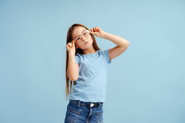 Funny little girl wearing stylish eyeglasses, looking at camera, having fun isolated on blue background. Childhood concept  - Photo, Image