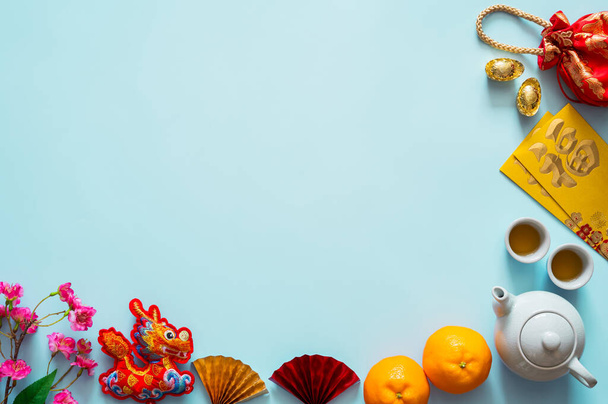 Chiński nowy rok tło z zestawem herbaty, pakiety kopert lub ang bao (słowo oznacza błogosławieństwo), czerwona torba, sztabki (słowo oznacza bogactwo), wiszący smok i pomarańcze wiszące na niebieskim tle - Zdjęcie, obraz