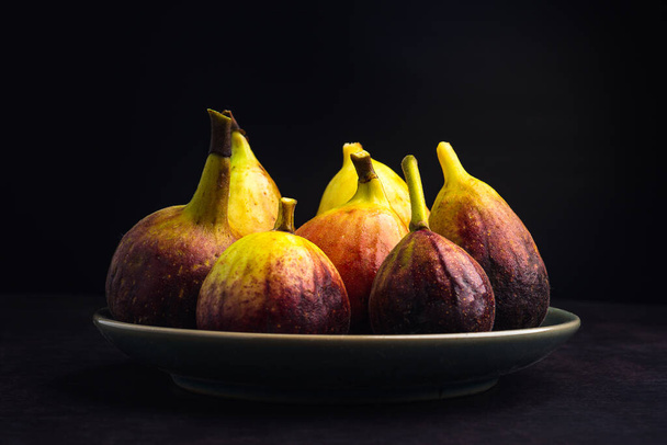 Pile of ripe figs fruit are on a plate with black background. High Vitamins fruit. Close-up photo. Healthy fruits and healthcare concept. - Photo, Image