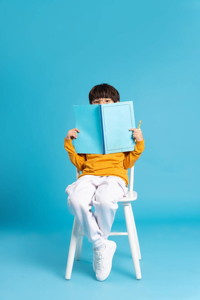 Mavi arka planda izole edilmiş oturan bir çocuğun portresi. - Fotoğraf, Görsel