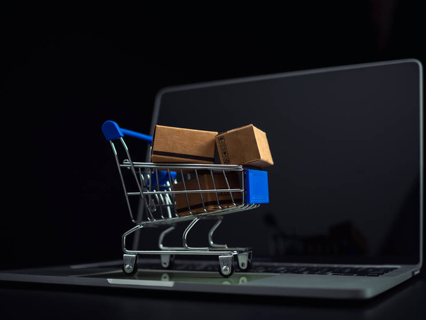 Dobozok egy bevásárlókocsiban egy laptop billentyűzetén. Ötletek az online vásárlásról, az online vásárlásról az elektronikus kereskedelem egy formája, amely lehetővé teszi a fogyasztók számára, hogy közvetlenül vásároljanak az eladótól az interneten keresztül. - Fotó, kép