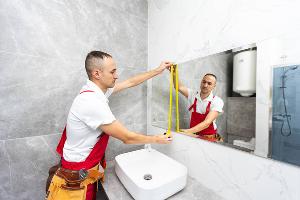 Homme installant un miroir sur le mur dans sa salle de bain renouvelée. Photo de haute qualité - Photo, image
