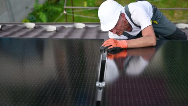 Napelemes rendszert építő munkások a ház tetején. Férfi mérnök sisakban beszerelése fotovoltaikus napelem modul a szabadban. Alternatív, zöld és megújuló energiatermelési koncepció. - Felvétel, videó