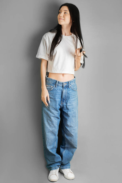 Full length portret van een jonge tiener meisje in een wit T-shirt en jeans. - Foto, afbeelding