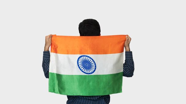 Вид ззаду молодого індійця, який з гордістю демонструє індійський прапор, тримаючи в руці національний прапор, під час фестивалю 26 січня Індії, ізольований білий фон. - Фото, зображення