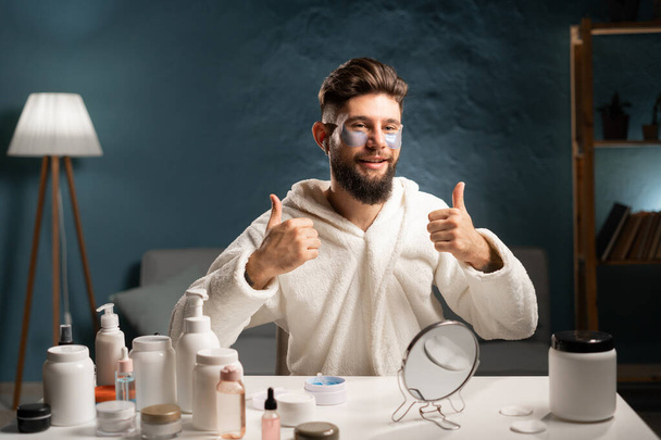 Handsome bearded man wears bathrobe recommended collagen patches under eyes, looking at camera doing daily evening beauty routine. beauty, skin care and people concept - Photo, Image