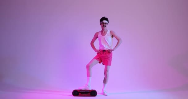 Charismatique homme caucasien, orné d'une moustache, danse avec exubérance aux côtés d'un lecteur de cassettes classique sur un fond violet captivant. Cette scène animée capture l'esprit rétro. - Séquence, vidéo