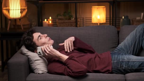 Az energikus kaukázusi férfi telefonbeszélgetést folytat, miközben a kanapén fekszik. A jelenet megragadja a kommunikáció dinamikus pillanatát, ötvözi a tevékenységet az otthon kényelmével. - Felvétel, videó