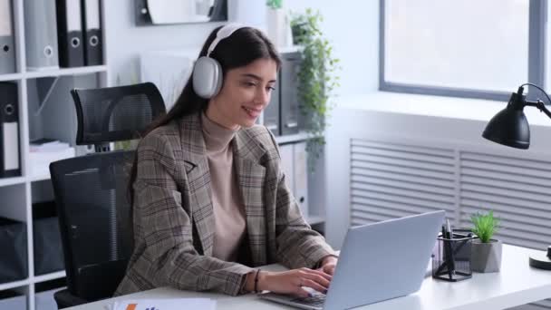 Empresária em fones de ouvido saboreia música durante o trabalho no escritório. Essa imagem capta os momentos positivos e prazerosos que ela incorpora na rotina profissional. - Filmagem, Vídeo