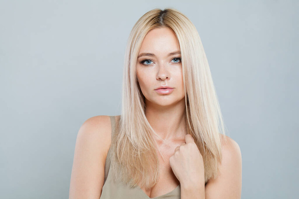 Herrliche blonde Frau mit langen glatten Haaren und sauberer, reiner, perfekter Haut isoliert auf grauem Hintergrund, Studioporträt - Foto, Bild