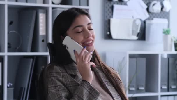 Kahkaha atan beyaz kadın ofiste bir telefon görüşmesi yapıyor. Bu görüntü, neşeli ve neşeli bir anı yakalar. Olumlu iletişim ve dostluk atmosferini gözler önüne serer.. - Video, Çekim