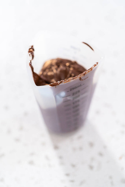 チョコレートで覆われたプレッツェルロッドを作るためにキャンディー溶融ポットでチョコレートチップを溶融. - 写真・画像