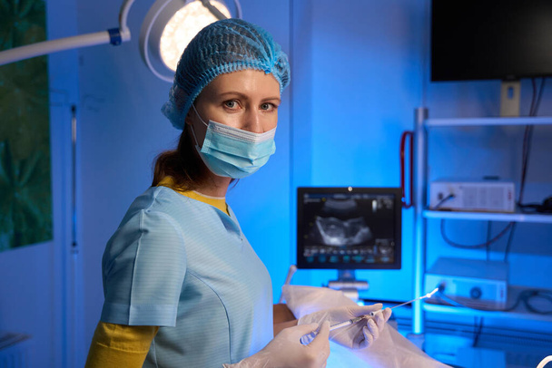 Gedeeltelijk bijzicht van vrouwelijke arts met injectiespuit voor embryotransfer en kijkend naar de camera in de voortplantingskliniek. Embryologie en biotechnologie - Foto, afbeelding