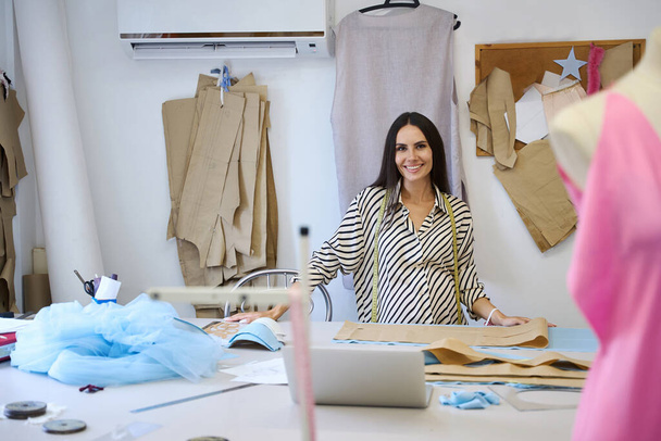 Ambachtelijke vrouw in een gestreepte blouse op haar werkplek aan de snijtafel, ze maakt gebruik van een papieren patroon - Foto, afbeelding