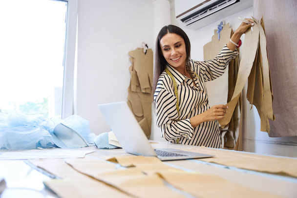 縫製スタジオの職場で妊娠中の女性,彼女は彼女の仕事でラップトップとパターンを使用しています - 写真・画像