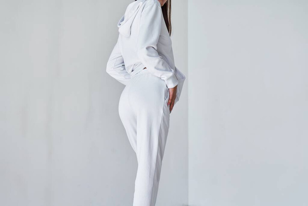 Ervaar de ultieme casual stijl met dit Contemporary White Ensemble. Sportwear mock-up. Een meisje in een witte broek. Achteraanzicht van een jonge vrouw in een witte minimalistische joggingbroek. - Foto, afbeelding