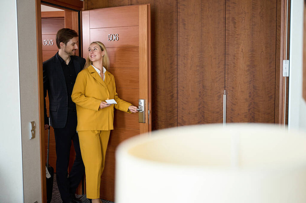 Mosolygó férfi és nő bemennek a hotelszobába, miközben egymásra néznek. - Fotó, kép