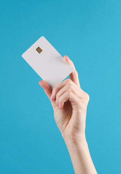 Kobieta trzyma białą, pustą kartę bankową z chipem na niebieskim tle. Układ, makieta, szablon do projektowania - Zdjęcie, obraz