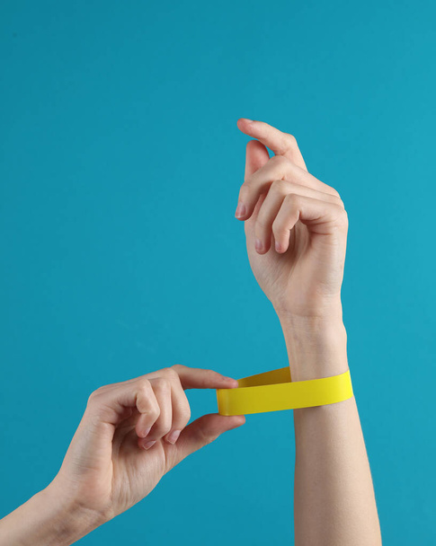 Female hand with a yellow paper bracelet on a blue background - Photo, Image