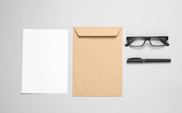 Ремесленный почтовый конверт с белым пустым письмом, очками и ручкой на сером фоне. Концепция бизнеса - Фото, изображение