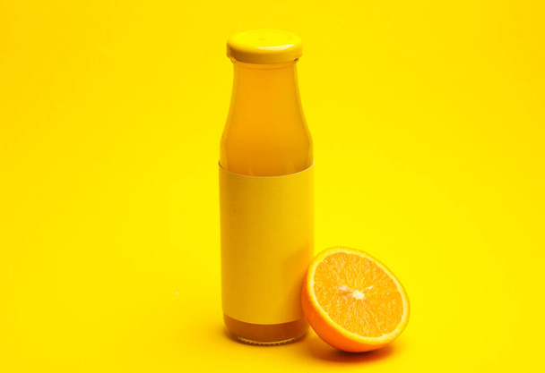 Botella de zumo de naranja con media naranja jugosa sobre fondo amarillo - Foto, Imagen