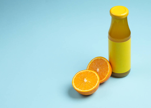 Bottiglia di succo d'arancia con mezza arancia succosa su sfondo blu - Foto, immagini