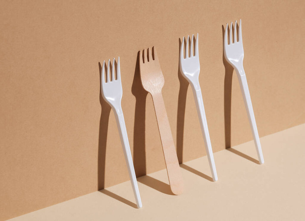 Plastic and wooden forks on a beige background with a shadow. Eco concept, plastic free, food. Creative layout - Photo, Image