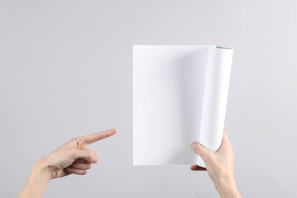 Γυναικεία χέρια κρατούν ένα κενό περιοδικό mockup με λευκές σελίδες σε γκρι φόντο - Φωτογραφία, εικόνα