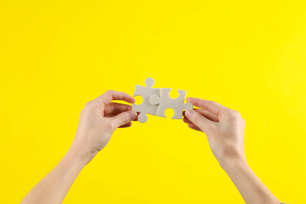 Las manos de la mujer sostienen piezas de rompecabezas sobre un fondo amarillo. Concepto de negocio, trabajo en equipo - Foto, imagen