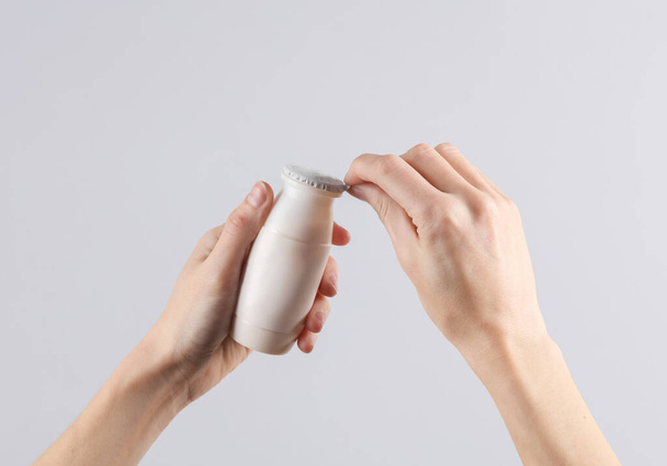 As mãos femininas abrem uma garrafa de iogurte em um fundo cinza - Foto, Imagem