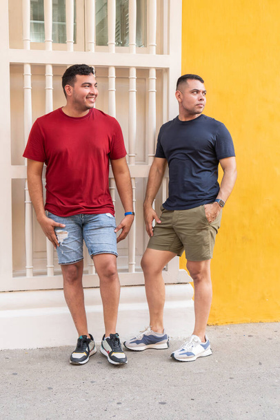 Zwei Männer in lässiger Sommerkleidung unterhalten sich beim Spazierengehen auf einer Stadtstraße - Foto, Bild