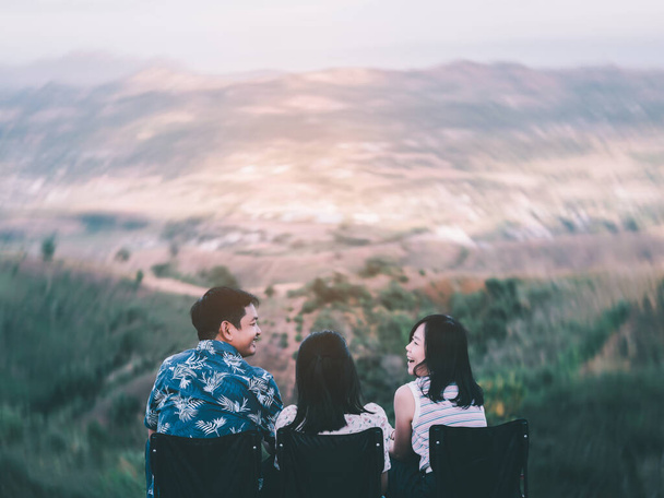 Parents and children sit on lawn chairs at the top of the mountain on vacation. A happy family talks on the top of the mountain and laughs happily together - Photo, Image