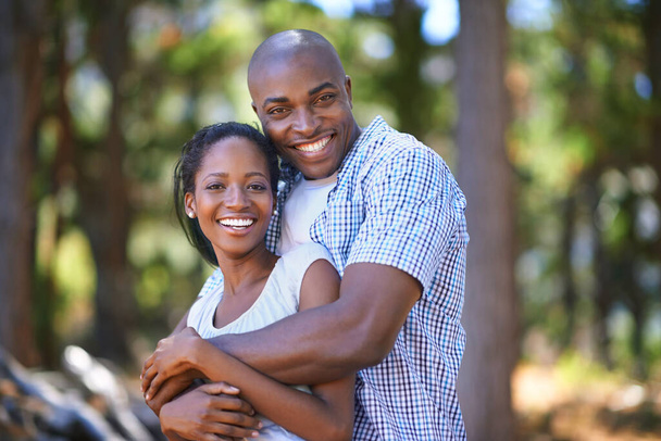 Hug, portrait or black couple hiking in forest to relax or bond on holiday vacation together in nature. Happy, travel or African woman with smile or man in woods trekking on outdoor park adventure. - Photo, Image